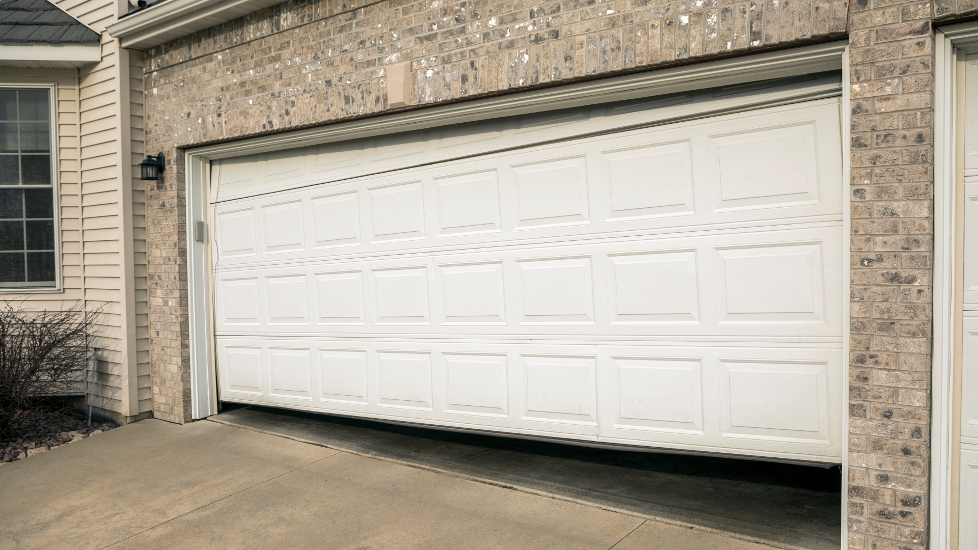 Misaligned garage door with a large gap at the bottom due to track or spring issues.