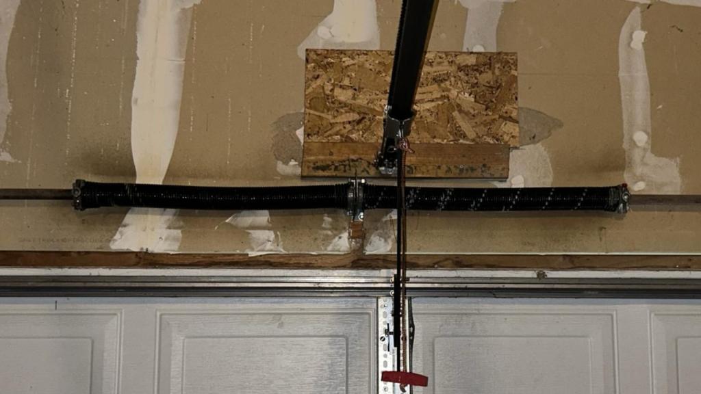Close-up view of a black torsion garage door spring installed above a white double garage door in a Denver home